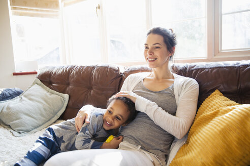 Liebevolle Mutter und ihr kleiner Sohn kuscheln auf dem Wohnzimmersofa - HOXF03898