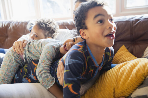 Verspielte, liebevolle junge Familie im Pyjama auf dem Wohnzimmersofa - HOXF03901