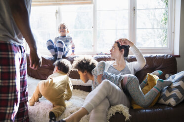 Multiethnische junge Familie im Schlafanzug spielt im sonnigen Wohnzimmer - HOXF03910