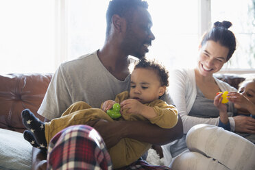 Happy multi-ethnic family in pajamas cuddling on sofa - HOXF03912