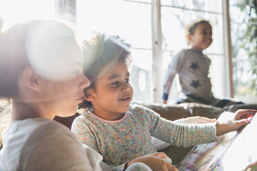 Mutter und Tochter lesen ein Buch im sonnigen Wohnzimmer - HOXF03923