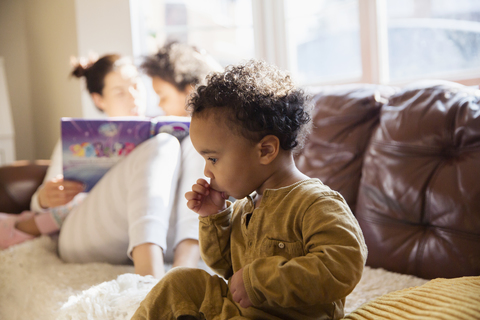 Unschuldiges Baby auf dem Sofa lutscht am Daumen, lizenzfreies Stockfoto