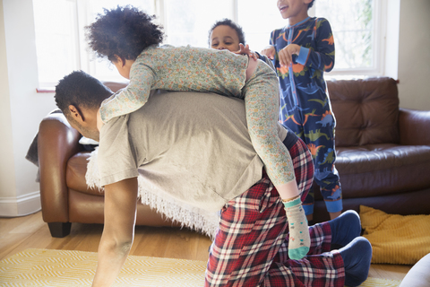 Verspielter Vater im Pyjama, der seine Tochter auf dem Rücken trägt, lizenzfreies Stockfoto