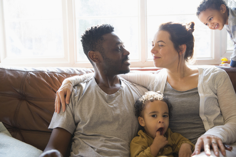 Liebevolle multiethnische junge Familie auf dem Wohnzimmersofa, lizenzfreies Stockfoto