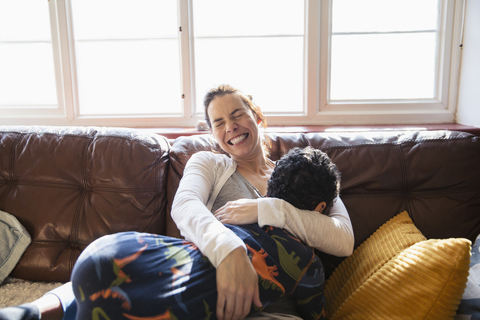 Glückliche, sorglose Mutter kuschelt mit ihrem Sohn auf dem Wohnzimmersofa, lizenzfreies Stockfoto