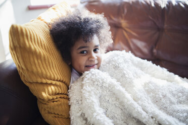 Portrait süßes Mädchen entspannt, kuschelnd auf Sofa mit Decke und Kissen - HOXF03940