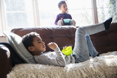 Brüder entspannen sich, sehen fern und genießen einen Snack auf dem Sofa im Wohnzimmer - HOXF03943