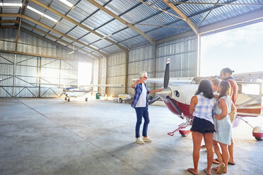 Pilot im Gespräch mit Freunden an einem Propellerflugzeug in einem Flugzeughangar - CAIF21753