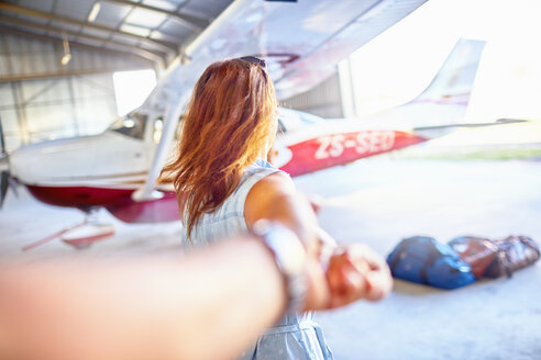 Persönliche Perspektive Frau führt Mann an der Hand zu kleinem Flugzeug in Flugzeughangar - CAIF21761