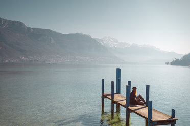 Frau sitzt auf einem Steg am Seeufer, Annecy, Haute-Savoie, Frankreich - AURF04013
