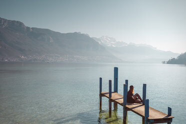 Woman sitting on jetty on lakeshore, Annecy, Haute-Savoie, France - AURF04013