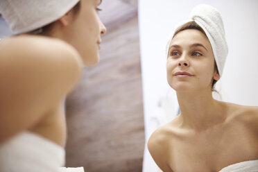 Mirror image of young woman examining her face in the bathroom - ABIF00983