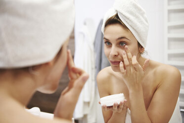 Mirror image of young woman applying moisturizer in bathroom - ABIF00986