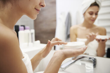 Young woman applying moisturizer in bathroom, partial view - ABIF00987