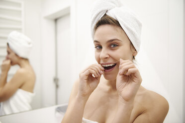 Portrait of young woman using dental floss in bathroom - ABIF00989