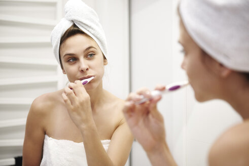 Mirror image of young woman in bathroom brushing her teeth - ABIF00990