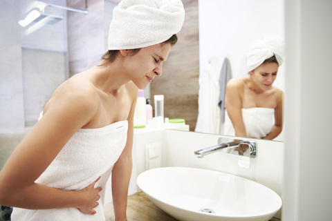 Junge Frau im Badezimmer mit Bauchschmerzen, lizenzfreies Stockfoto