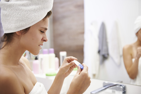 Junge Frau im Badezimmer, die sich Sorgen um das Ergebnis eines Schwangerschaftstests macht, lizenzfreies Stockfoto