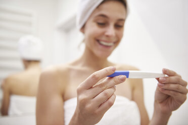 Hände einer glücklichen jungen Frau mit Schwangerschaftstest im Badezimmer - ABIF00997