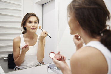 Spiegelbild einer lächelnden jungen Frau, die im Badezimmer Make-up aufträgt - ABIF00999