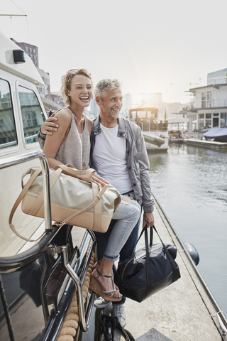 Älterer Mann und junge Frau stehen mit Reisetaschen auf dem Steg neben einer Jacht, lizenzfreies Stockfoto