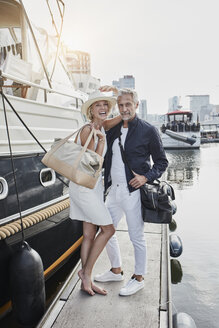 Older man and young woman standing with travelling bags on jetty next to yacht - RORF01555