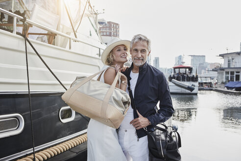 Older man and young woman standing with travelling bags on jetty next to yacht - RORF01556