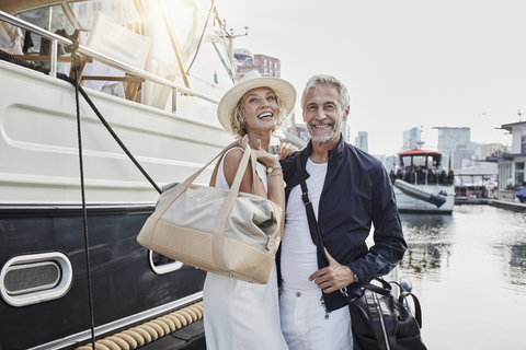 Älterer Mann und junge Frau stehen mit Reisetaschen auf dem Steg neben einer Jacht, lizenzfreies Stockfoto