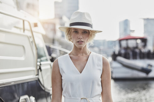 Porträt einer ernsten jungen Frau mit Hut in einem Jachthafen neben einer Yacht - RORF01560
