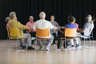 Active seniors meditating, holding hands in circle - CAIF21868