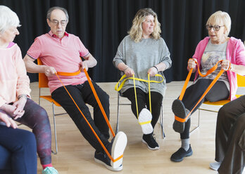 Aktive Senioren, die im Kreis trainieren und ihre Beine mit Hilfe von Bändern strecken - CAIF21871