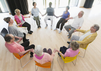 Aktive Senioren halten sich im Kreis an den Händen und meditieren im Gemeindezentrum - CAIF21886