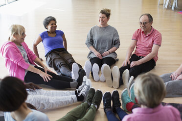 Kursleiter und aktive Senioren dehnen die Beine im Kreis in einem Sportkurs - CAIF21888