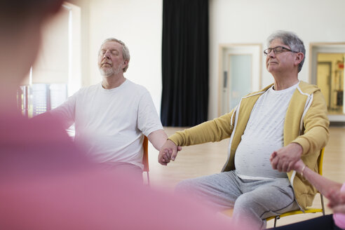 Gelassene aktive ältere Männer, die sich an den Händen halten und im Gemeindezentrum meditieren - CAIF21894