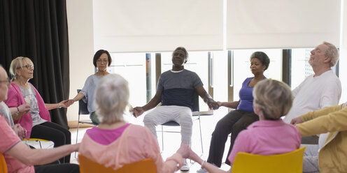 Serene active seniors holding hands, meditating in circle - CAIF21895