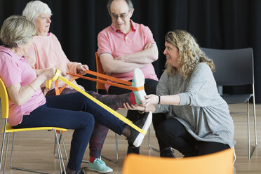 Instructor helping active seniors stretching legs, exercising with straps - CAIF21899