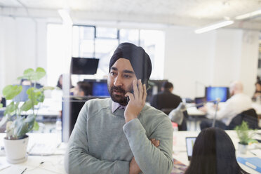 Seriöser indischer Geschäftsmann mit Turban, der im Büro mit einem Smartphone telefoniert - CAIF21916