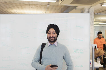 Porträt eines lächelnden, selbstbewussten indischen Geschäftsmannes mit Turban, der an einer Tafel im Büro steht - CAIF21920