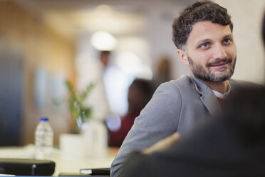 Smiling businessman listening to colleague in office - CAIF21923