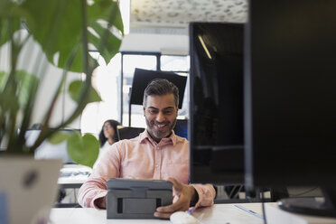 Lächelnder Geschäftsmann mit digitalem Tablet im Büro - CAIF21936