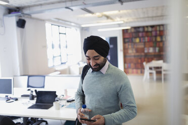 Indischer Geschäftsmann mit Turban benutzt ein Smartphone im Büro - CAIF21940