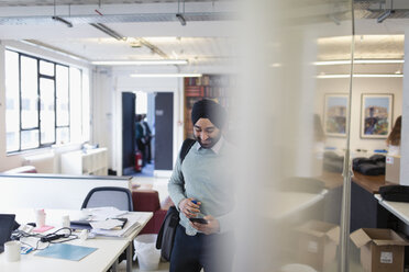 Indischer Geschäftsmann mit Turban benutzt ein Smartphone im Büro - CAIF21944