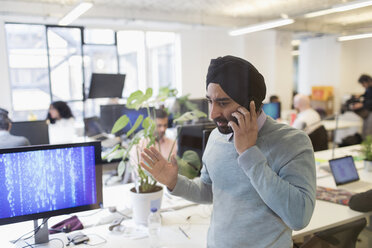 Indischer Computerprogrammierer mit Turban, der im Büro mit einem Smartphone telefoniert - CAIF21945