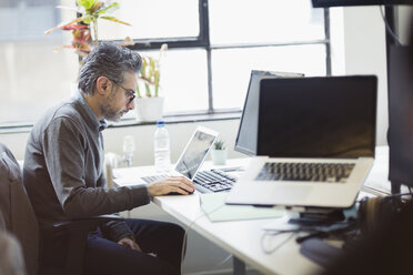 Konzentrierter Geschäftsmann bei der Arbeit am Laptop im Büro - CAIF21948