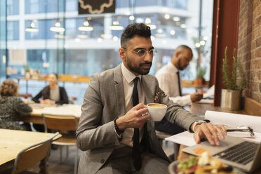 Konzentrierter Geschäftsmann trinkt Kaffee und arbeitet am Laptop in einem Café - CAIF21956