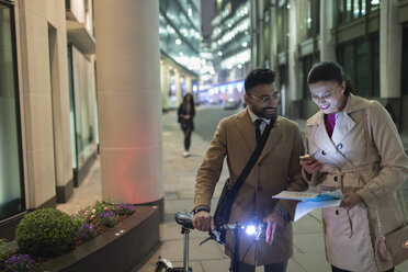 Geschäftsleute mit Smartphone und Fahrrad bei der Durchsicht von Papieren auf einer nächtlichen Stadtstraße - CAIF21959