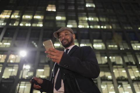 Geschäftsmann mit Smartphone unter städtischem Hochhaus bei Nacht, lizenzfreies Stockfoto
