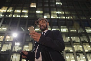 Geschäftsmann mit Smartphone unter städtischem Hochhaus bei Nacht - CAIF21960