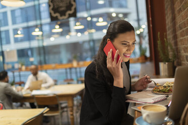 Lächelnde Geschäftsfrau, die mit einem Smartphone spricht und an einem Laptop im Café arbeitet - CAIF21963