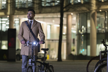 Geschäftsmann mit Fahrrad auf städtischer Straße bei Nacht - CAIF21973